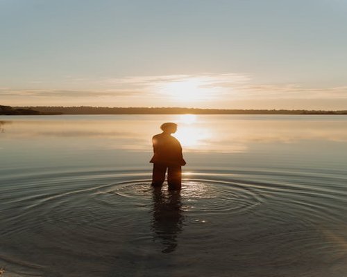 Person meditating by a calm lake at sunset